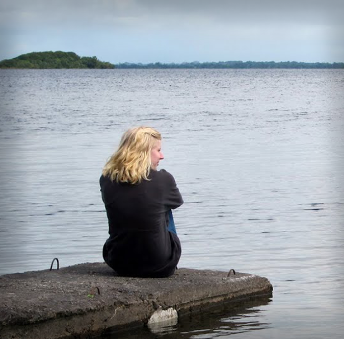 Solo female traveler sitting quietly on a lakeside dock reflecting on her surroundings